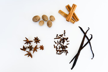 Spices used in cooking, often for Christmas baking, whole nutmeg, cinnamon sticks, vanilla beans, cloves and star anise. Flat lay isolated on white