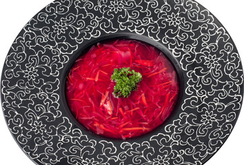 Plate of root soup borsch isolated on white background, top view. Black plate with a pattern