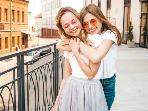 Portrait of two young beautiful blond smiling hipster girls in trendy summer white t-shirt clothes. Sexy carefree women posing on street background. Positive models having fun.Hugging