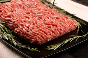 raw minced meat on paper, ingredients for burger with tomato, pepper, onion, spices and seasonings on black background