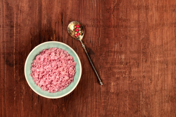 Obraz na płótnie Canvas A bowl of pink Himalayan sea salt with a pepper mix, shot from above on a dark wooden background with a place for text