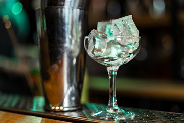 on the bar counter ice cubes in a glass next to a shaker