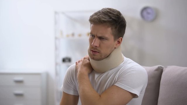 Upset man in foam cervical collar suffering pain in back and shoulder, injury