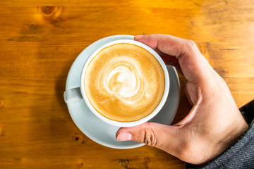 A cup of coffee in a cafe and a man's hands. Close-up of man's hands, sitting with cup of coffee, overhead