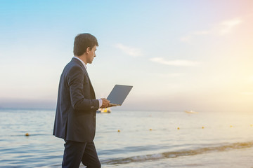 lateral view of a young man in suit with laptop working on the seaside