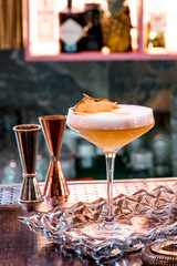 Yellow cocktail with white foam, decorated with a slice of dry pineapple, in an elegant glass in a restaurant against the background of the interior. Close-up. Space