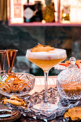 Yellow cocktail with white foam, decorated with a slice of dry pineapple, in an elegant glass in a restaurant against the background of the interior. Close-up. Space