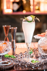 Beautiful white cocktail in elegant high glass on a crystal plate on the table in a restaurant on the background of the interior. Close-up. Space