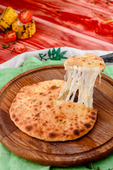Traditional Georgian dish - Khachapuri with cheese on a round wooden board on a red wooden background, decorated with napkins, chili pepper and cherry tomatoes. close-up