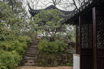China, Suzhou, Humble Government Park pavilion with red wood columns and black roof on the hill with stairs hidden in trees