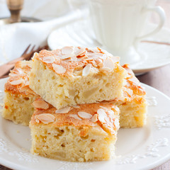 Sweet sliced apple pie with almond petals on a wooden table, square