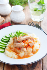 Pork with gravy and mashed potatoes and fresh cucumber on a wooden table, selective focus