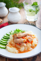 Pork with gravy and mashed potatoes and fresh cucumber on a wooden table, selective focus