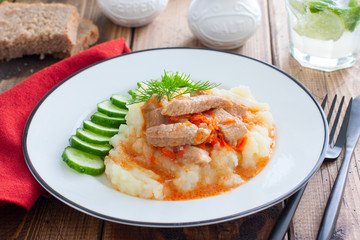 Pork slices with tomato sauce and mashed potatoes on a wooden table, horizontal