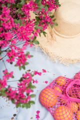 Pink flowers with thatch straw hat with oranges in pink bag