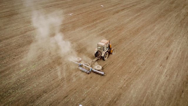 Aerial view on fast tractor with disc roller levels soil on field after sowing. Spring agricultural activities with heavy machinery