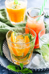 Cold orange with rosemary on a background of summer cold citrus drinks: mojito, lemonade, orange, mandarin juice and grapefruit, selective focus