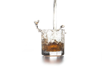Whiskey pouring into glass with ice on light background..