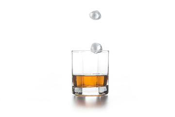 Whiskey splash from the fallen ice cube into glass with beverage on light background..