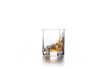 Whiskey splash in glass with ice on light background..