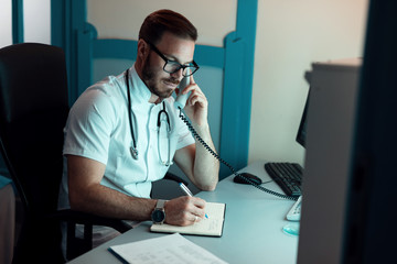 Doctor taking notes while talking on the phone in the office.