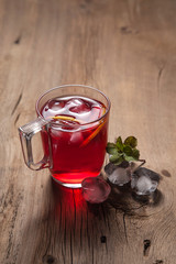 Hibiscus cold tea with ice and mint on vintage wooden background.