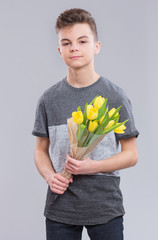 Holidays, Love, Happiness and People concept - Teen Boy holding Bouquet of Tulips, on gray background. Child has prepared Surprise for Mum or his Girlfriend - yellow Flowers.