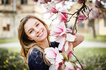 Beautiful blonde smiling woman posing with blooming magnolia in a park. © Michaela
