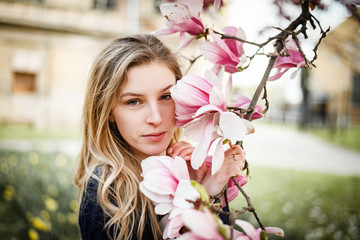 Fototapeta premium Blonde woman posing with magnolia in bloom looking in camera.