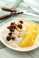 Plate with tasty mango and boiled rice on wooden table