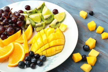 Plate with tasty mango and fresh fruits on wooden table