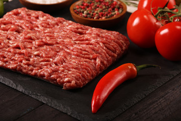 raw minced meat on plate, ingredients for burger with tomato, pepper, onion, spices and seasonings on black background.