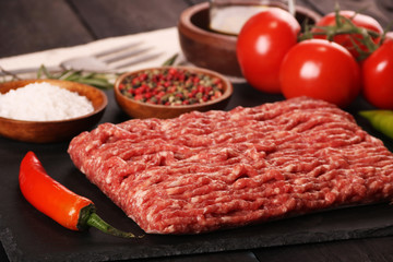 raw minced meat on plate, ingredients for burger with tomato, pepper, onion, spices and seasonings on black background.