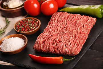 raw minced meat on plate, ingredients for burger with tomato, pepper, onion, spices and seasonings on black background.