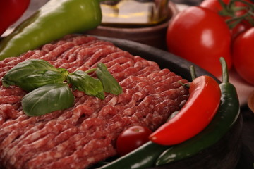 raw minced meat on plate, ingredients for burger with tomato, pepper, onion, spices and seasonings on black background.