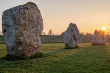Prehistoric standing rocks at a golden sunset and the sun dipping behind the rocks in a field in...