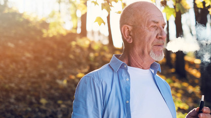 Close up portrait of senior man with a beard smiling while standing outside in sunlight.