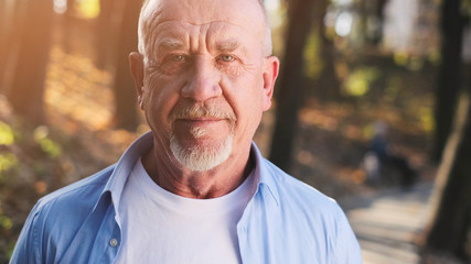 Portrait of senior man with a beard smiling while standing outside in sunlight.