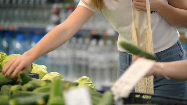 pretty girl woman picking veggies and fruits in supernarket in mesh organic shopping bag, zero waste , eco friendly