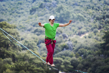 A man is walking along a stretched sling. Highline in the mountains. Man catches balance. Performance of a tightrope walker in nature. Highliner on the background of valley.