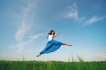 Flying dancer in the air. Happy woman ballerina in blue fabric skirt making a big jump on Green...