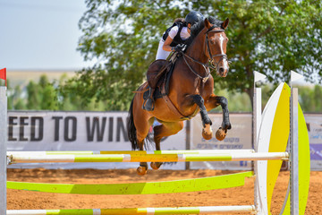 Young rider jumping over the obstacles during the horse jumping competition