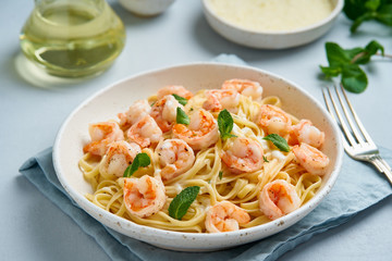 Pasta spaghetti with roasted shrimps, bechamel sauce, mint leaf on blue table, italian cuisine, side view