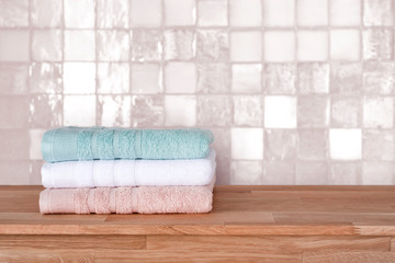 Obraz na płótnie Canvas Bath towel pile on wooden surface before ceramic tile wall