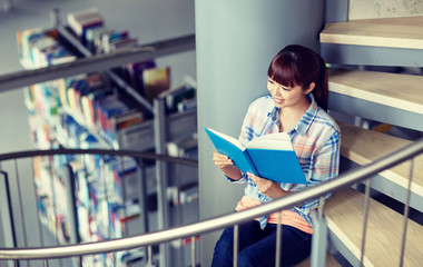 education, high school, university, learning and people concept - happy smiling asian student girl reading book sitting on stairs at library