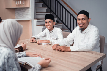 Obraz premium Portrait of muslim father and son sitting on table smiling to camera after reading quran