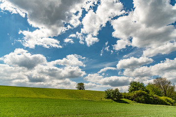 H&uuml;gelige Feldlandschaft mit wolkigem Himmel