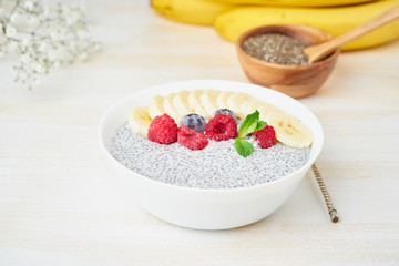 Chia pudding in bowl with fresh berries raspberries, blueberries. Side view, white wooden light background.
