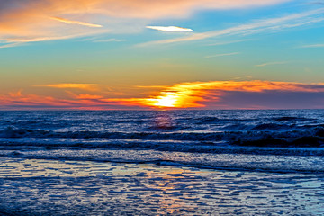 Sand beach with endless horizon and foamy waves under the bright sundown with yellow colors and clouds above the sea