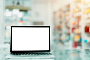 Laptop with blank screen on table with Pharmacy blurred with store drugs shelves interior...